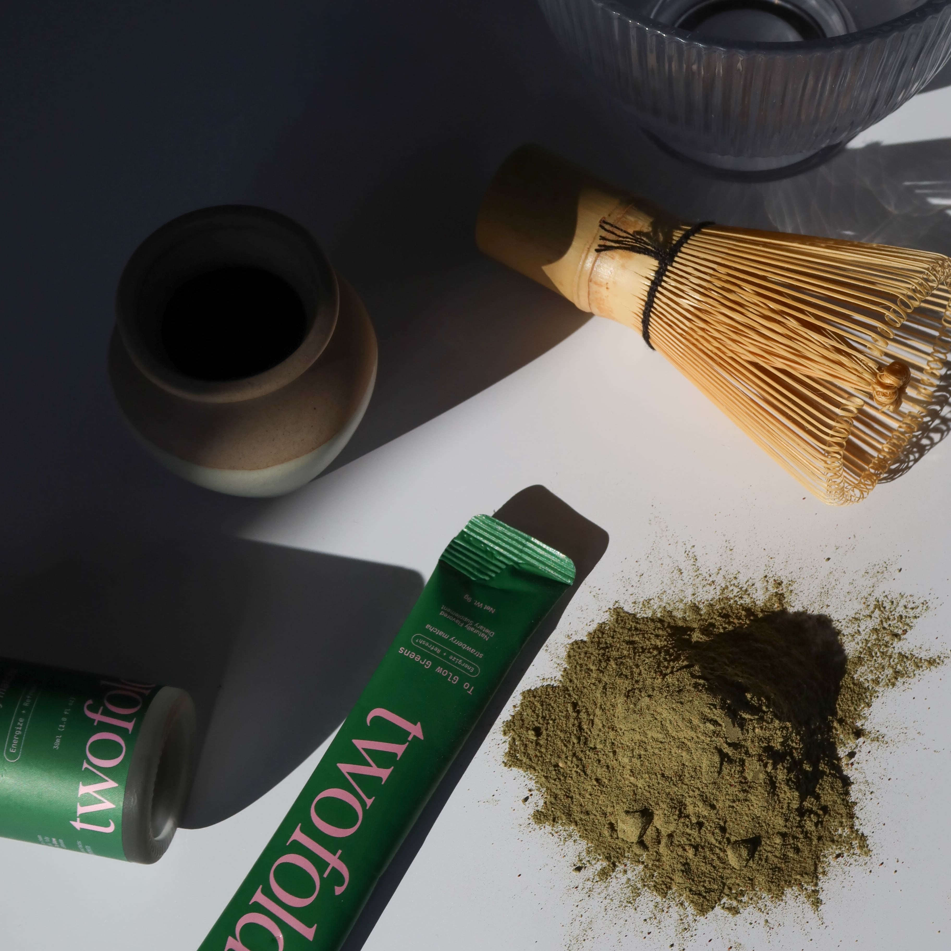 Matcha green tea powder with a whisk and container on a white surface