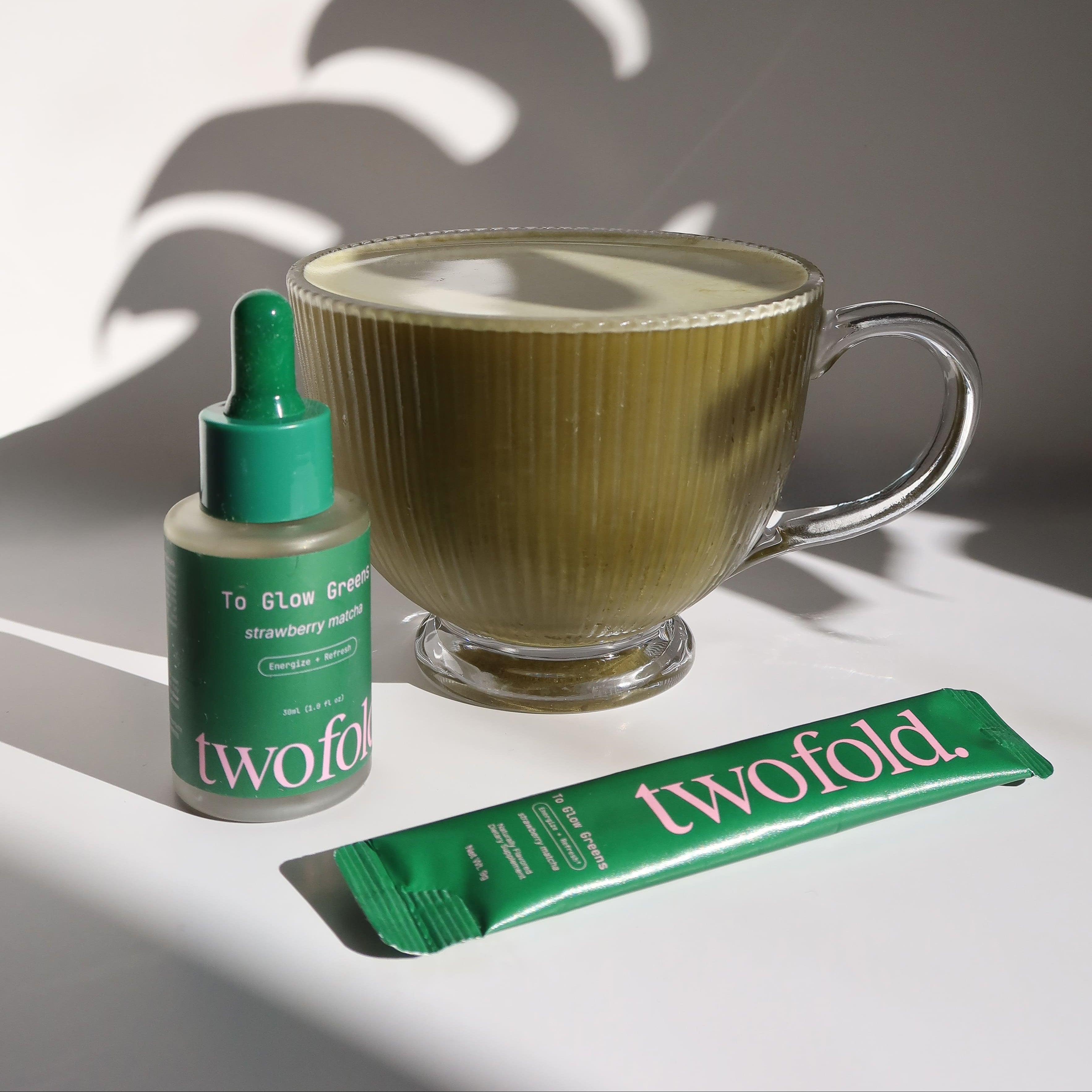 Twofold product packaging including a bottle, dropper, and a packet next to a cup of matcha green tea.