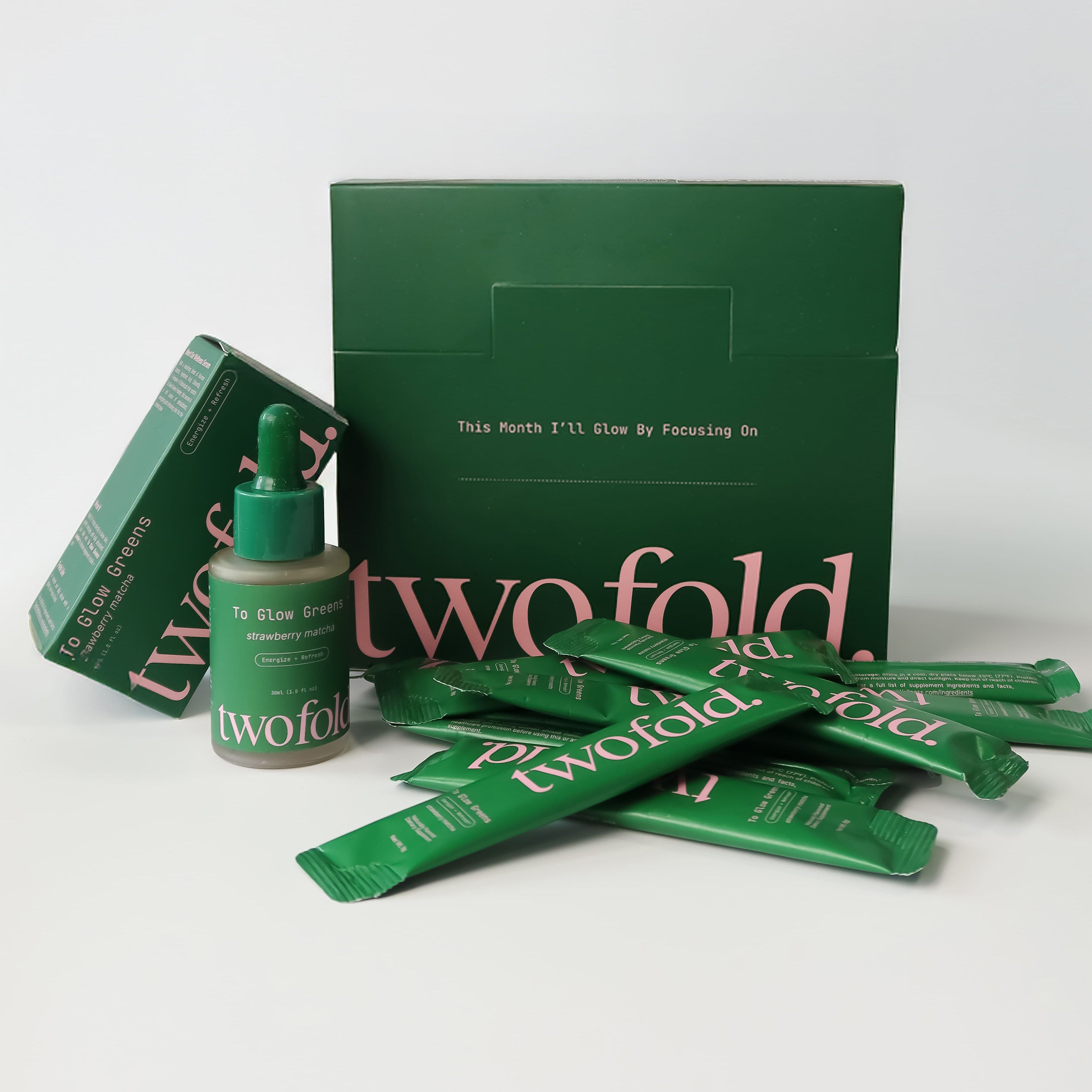 Green 'twofold' product packaging including a box, bottle, and packets on a white background